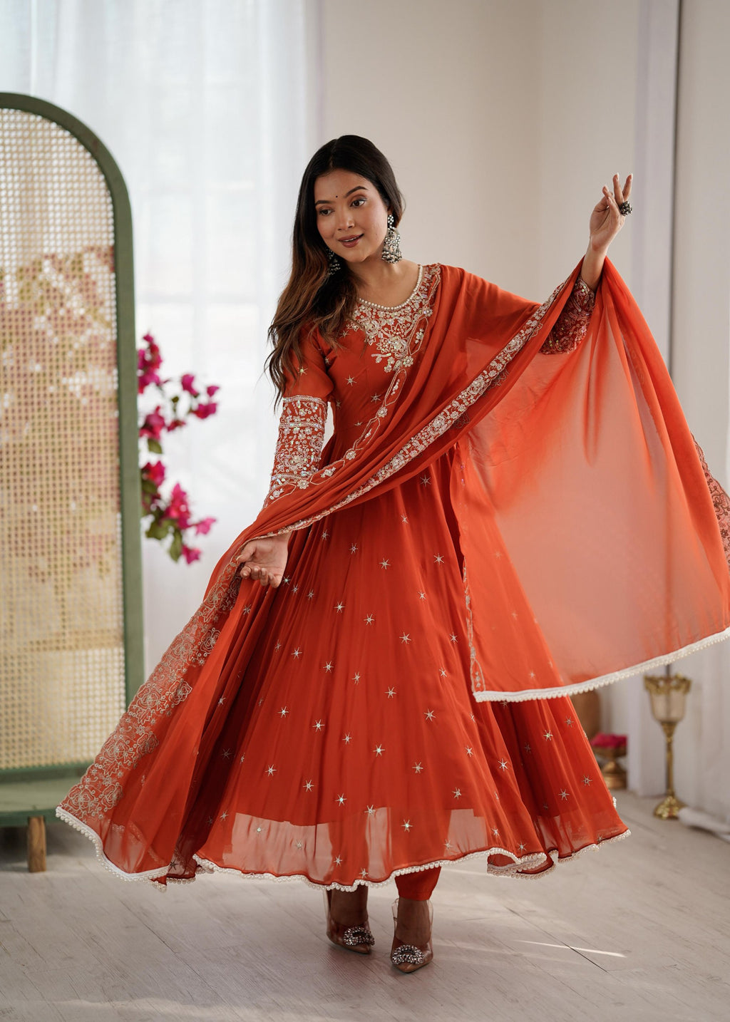 Full shot of a model twirling in an orange embroidered Anarkali gown with full sleeves and dupatta.