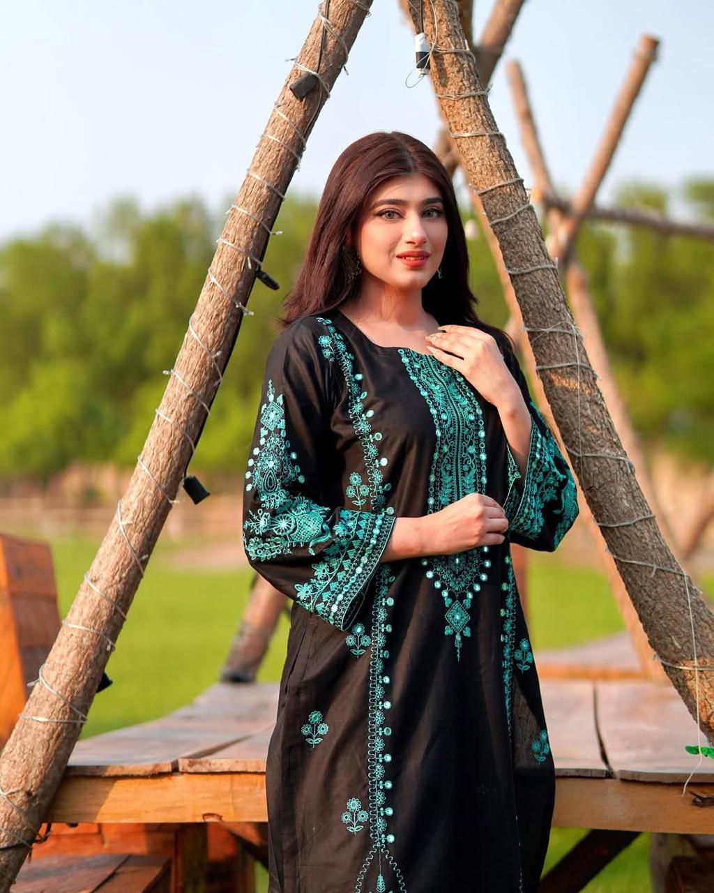 Model in black Roman silk kurta with teal embroidery and mirror work, outdoors.