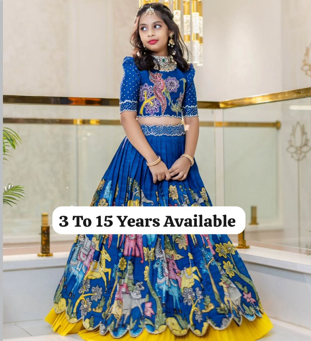 Young girl modeling a blue designer lehenga choli set with colorful animal and floral print, gold jewelry, showcasing the outfit's elegance.