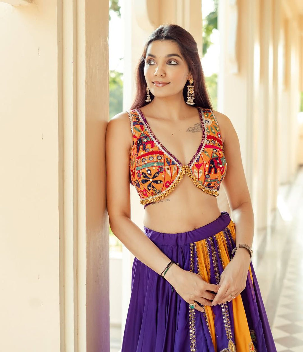 Elegant woman posing in a vibrant orange and purple mirror work choli, part of a Navratri special lehenga choli set.