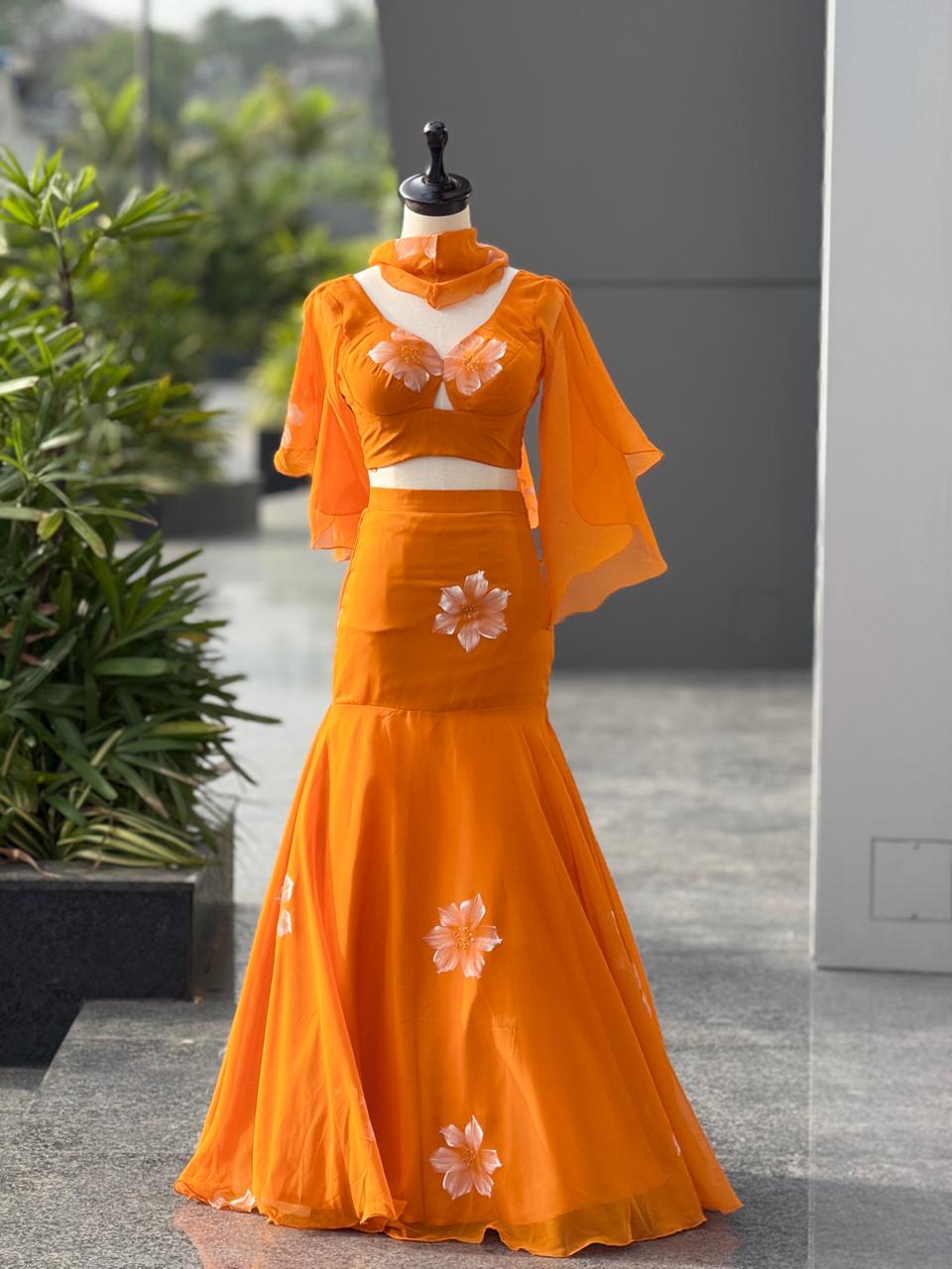 TRENDBUY Handpainted Georgette Fishcut Lehenga Choli Set in vibrant orange, showcasing the full ensemble with ruffle sleeve blouse and cascade dupatta, on a mannequin outdoors.