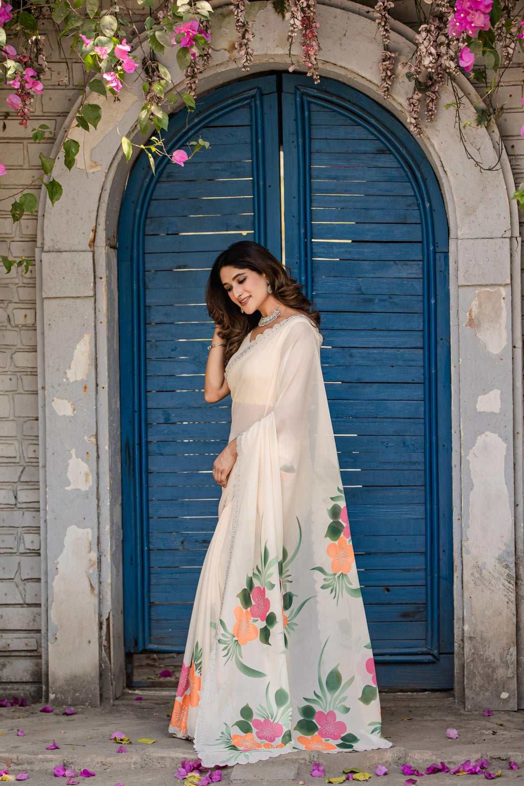 TRENDBUY model in off-white faux georgette saree with orange and pink floral digital print, posing by a blue door.