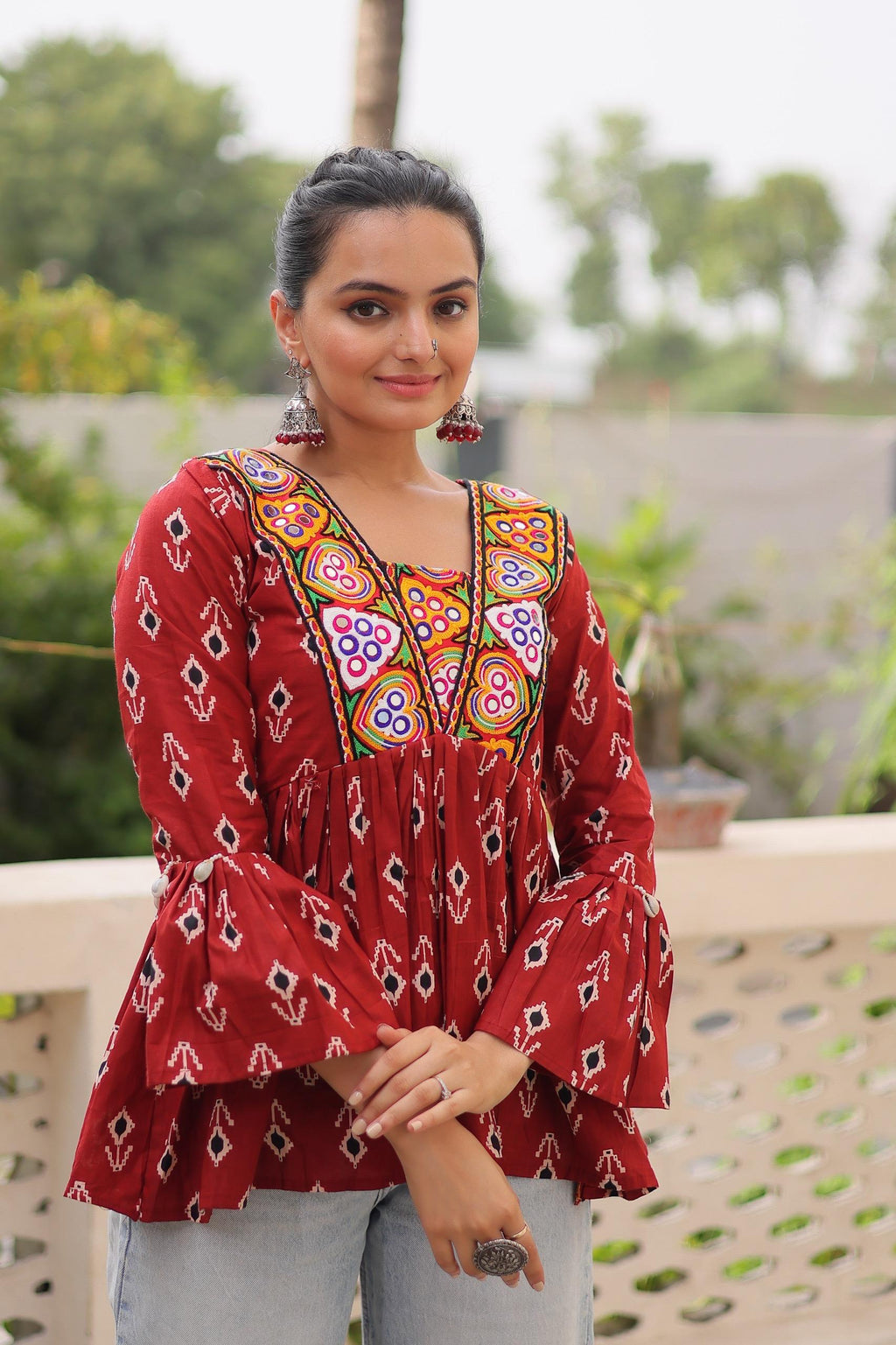 Model smiling in a maroon Kutchi patchwork peplum top with bell sleeves, posing frontally outdoors.