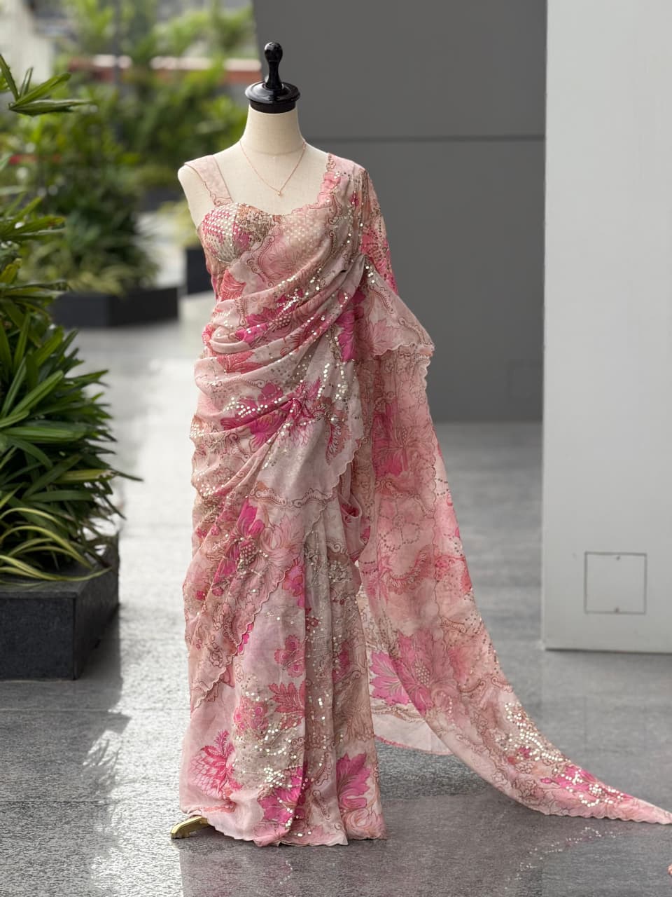 Full view of an elegant pink Jimmy Organza saree with digital prints and sequin work draped on a mannequin outdoors.
