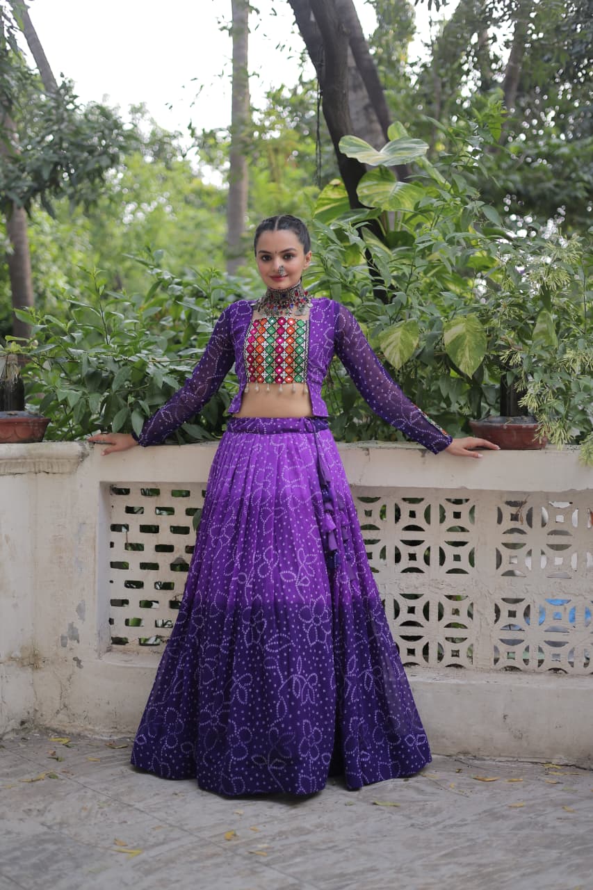 Full shot of model in purple Bandhani print lehenga choli with Kutchi Gamthi patchwork, leaning against a white railing amidst greenery.