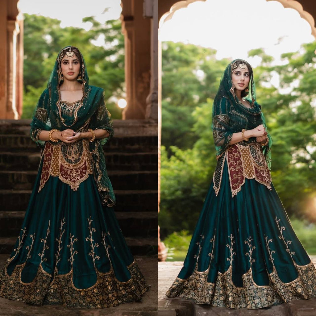 Model posing in an elegant emerald green crep silk lehenga choli set with rich embroidery and a sheer dupatta, in an archway.
