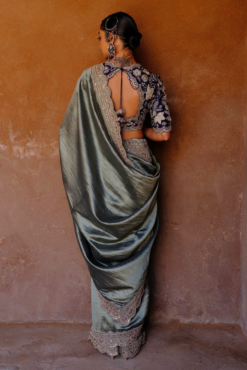 Rear view of model draped in a sage green crush saree, showcasing the intricate embroidery on the navy velvet backless blouse.