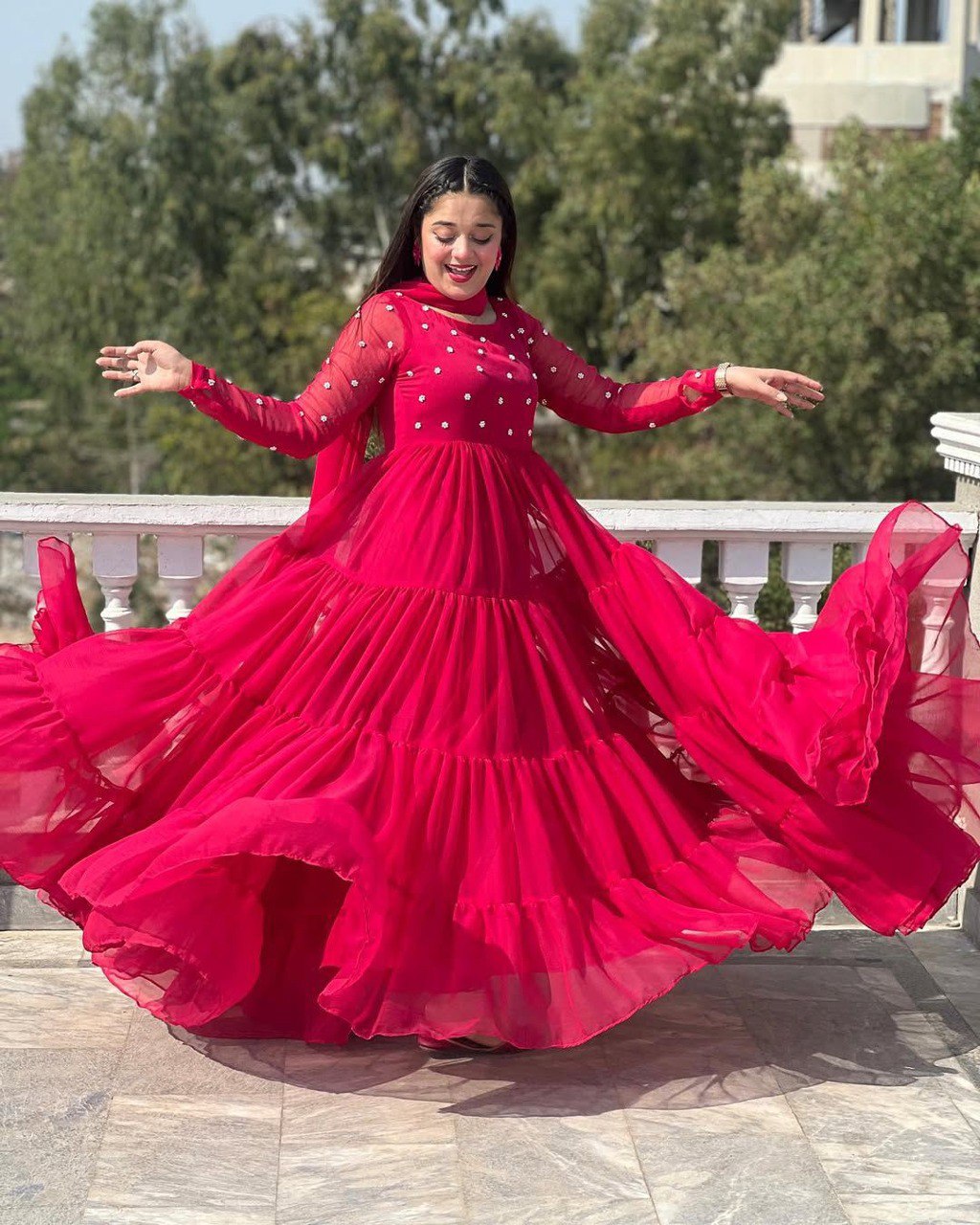 Young woman happily twirling in a vibrant red georgette gown with beadwork, showcasing its wide flair outdoors.