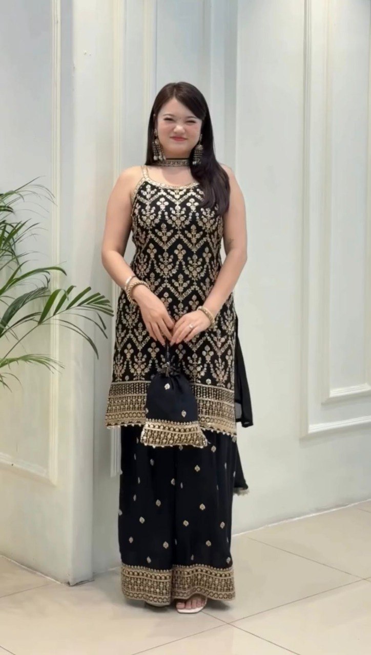 TRENDBUY model gracefully posing in a black faux georgette sharara suit with golden embroidery and matching potli bag.