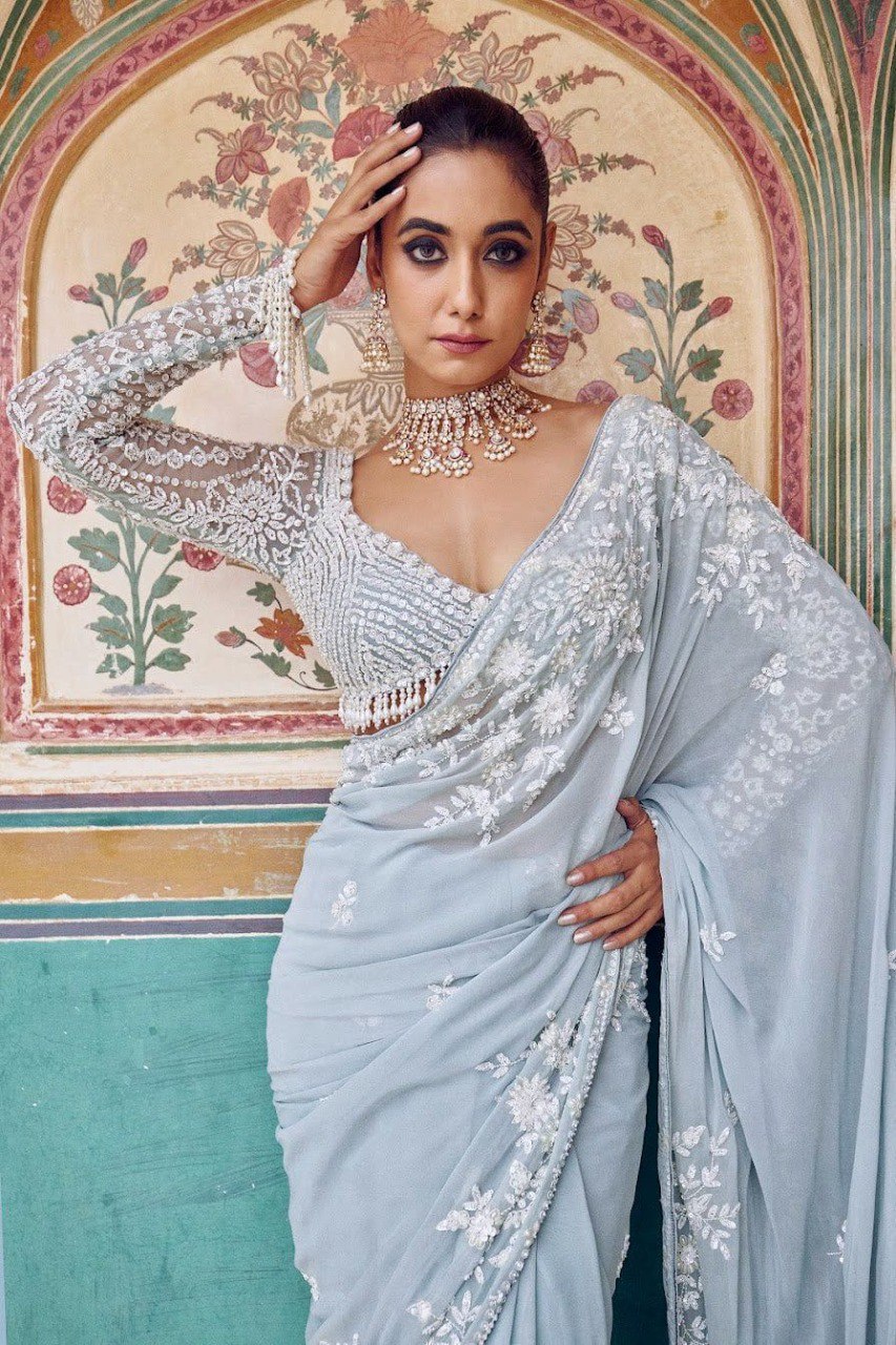 Close-up of a woman modeling the light blue Georgette saree, highlighting the delicate thread embroidery and sequin embellishments on the saree and long-sleeved blouse.