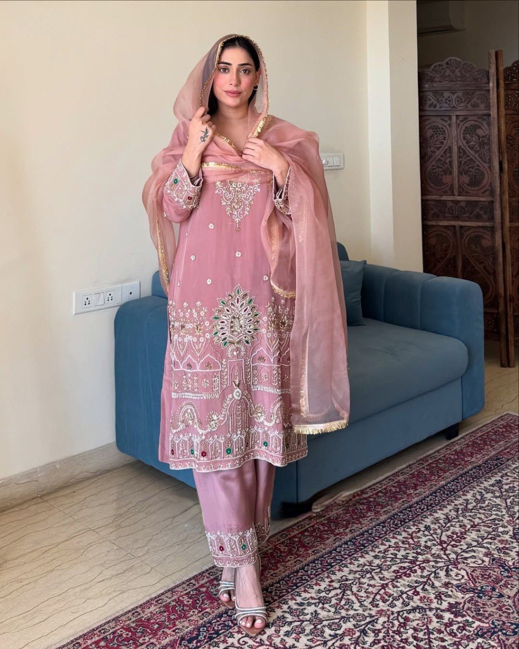 Model wearing a pink embroidered French crape 3-piece suit with organza dupatta, elegant full view indoors.