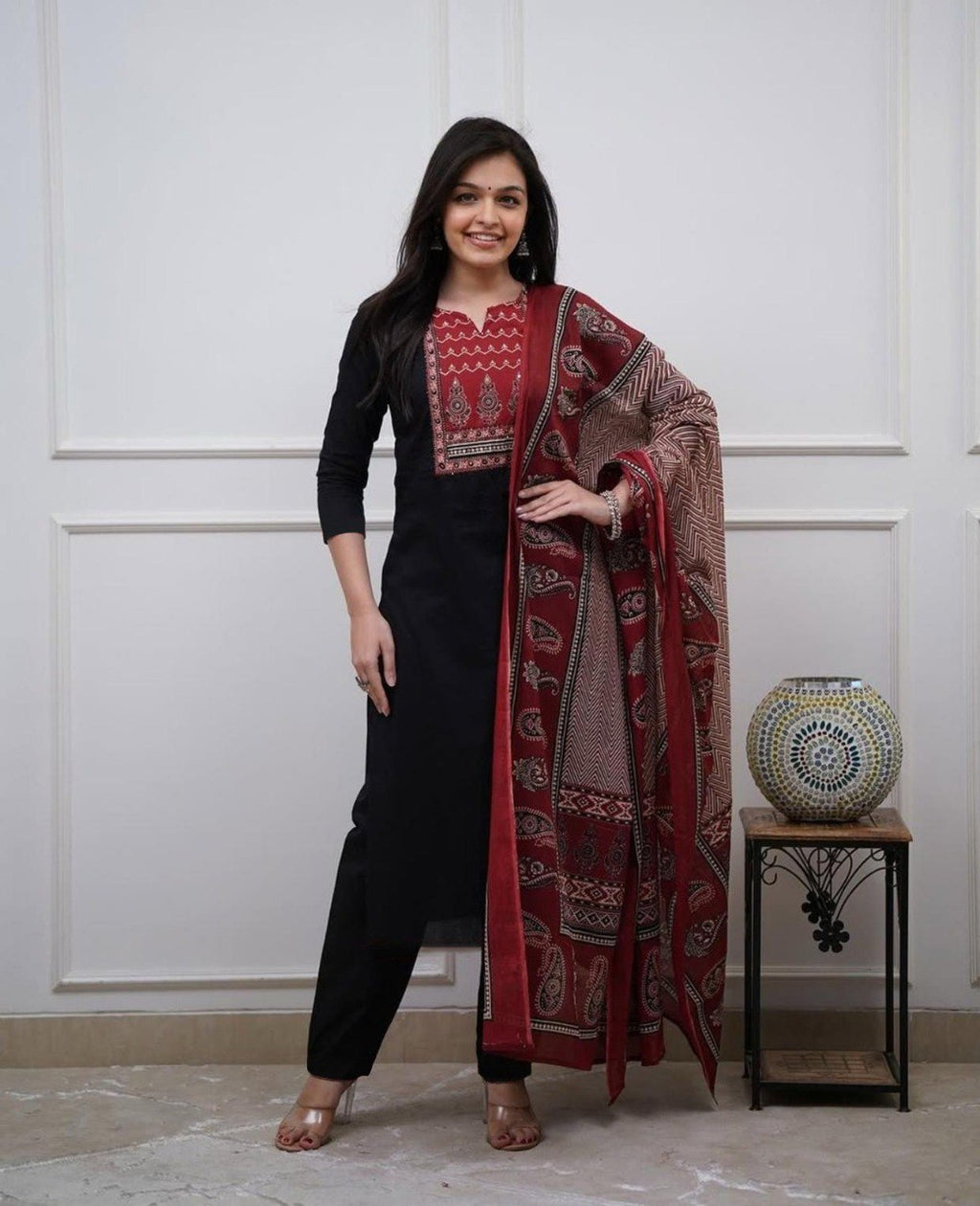 Smiling woman in full-length, posing in a black Rayon kurti, pant, and red-patterned maslin dupatta.