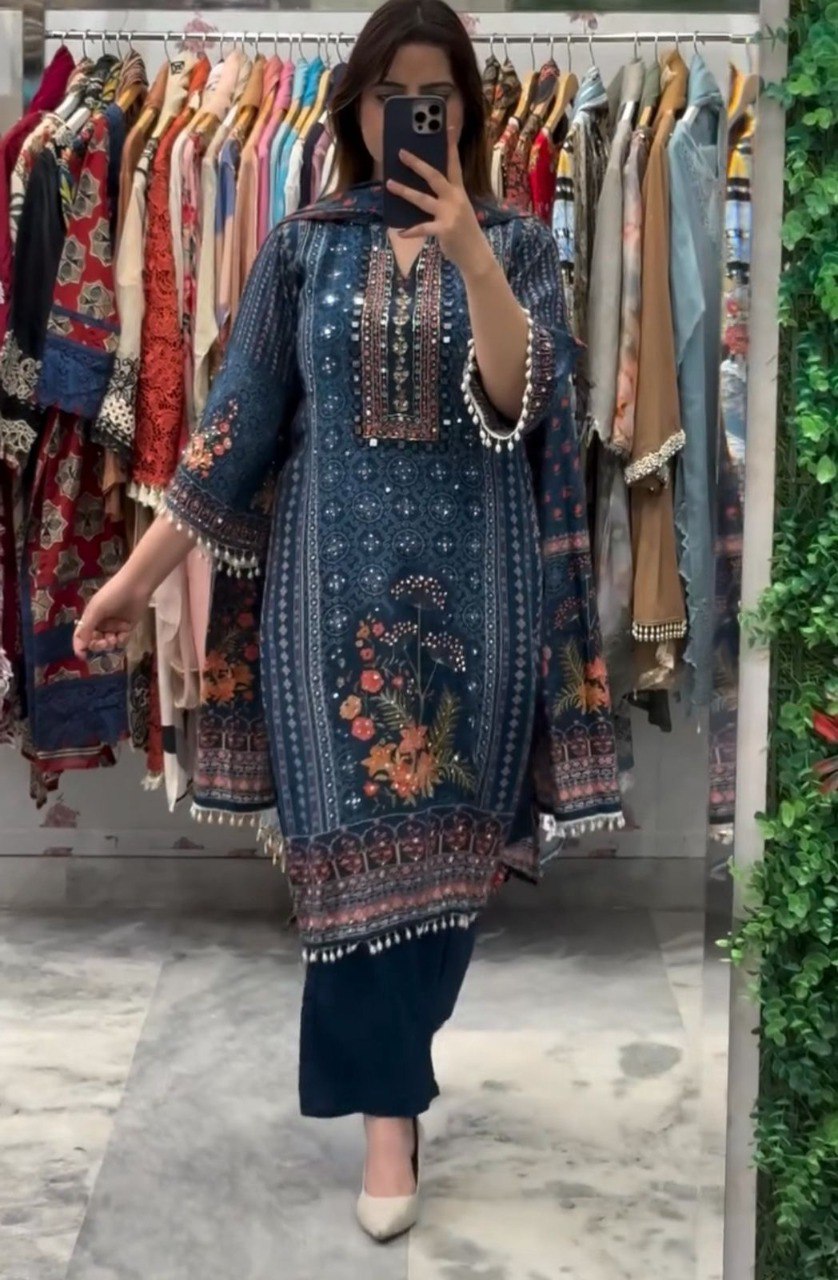 Full-length model shot of blue Chinon printed salwar suit with mirror work, standing against a clothing rack.