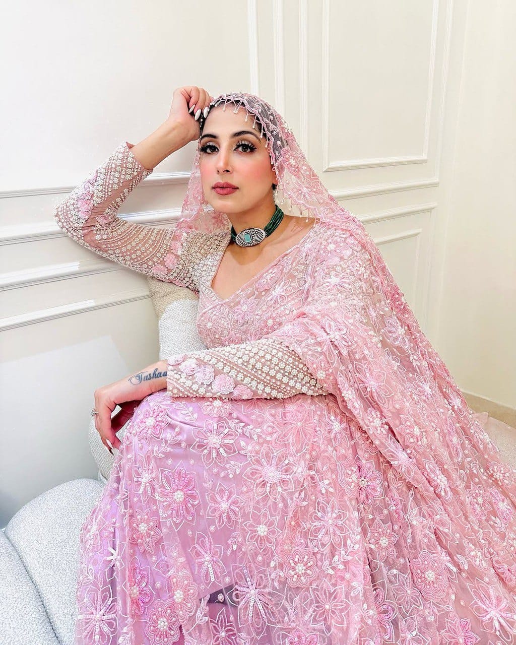 Elegant woman in a light pink butterfly net saree with intricate sequin and thread embroidery, posing gracefully.