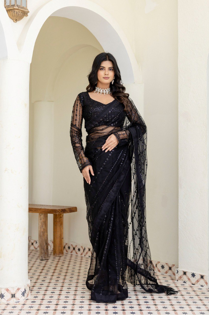 Full shot of woman in black sequin mono net saree, elegant pose in arched doorway.