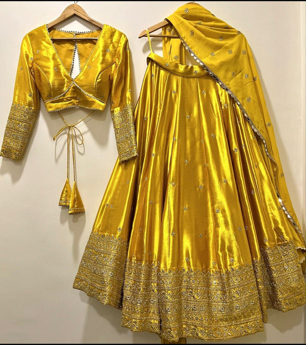 Golden Yellow Cinon-Silk Lehenga Choli Dupatta set with intricate sequence embroidery, displayed on hangers against a white wall.