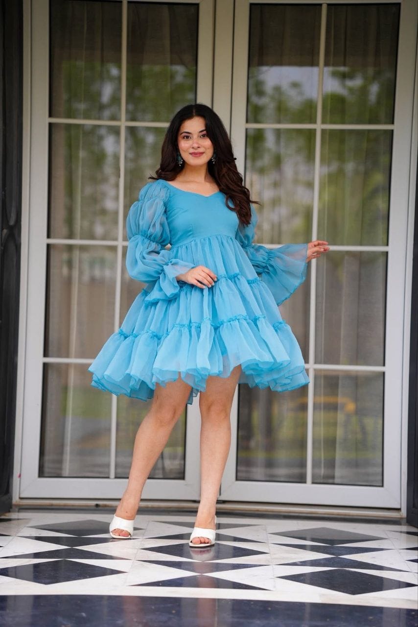 Stylish woman posing in front of white doors wearing a blue tiered mini dress with puff sleeves, front view.
