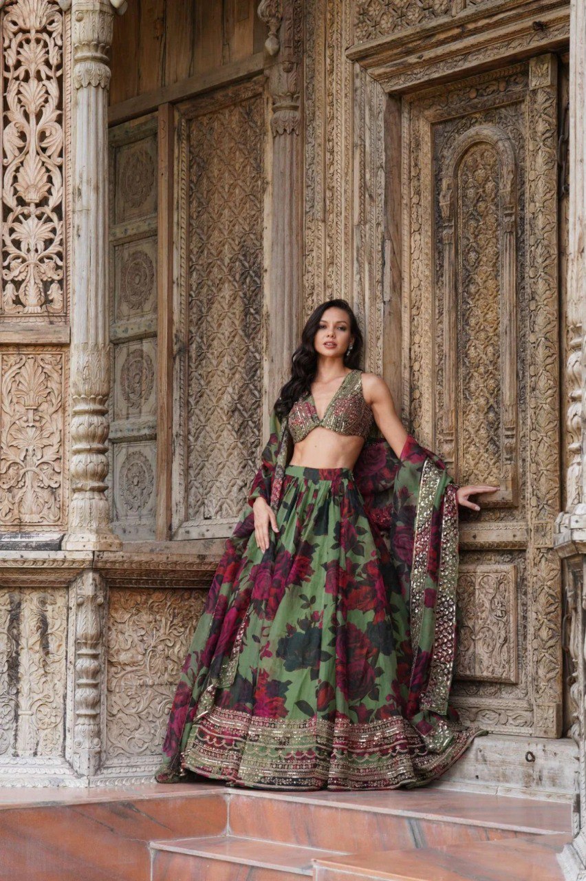 Graceful model posing in a green floral organza lehenga set with zari and sequin work against an ornate carved wooden door.