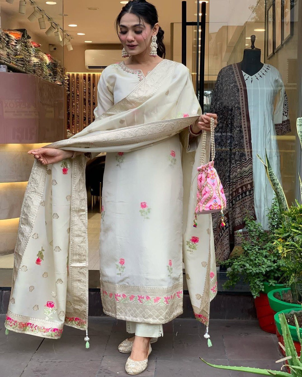 Model posing elegantly in a cream shimmer jacquard kurta set, showcasing the dupatta and holding a pink potli bag.