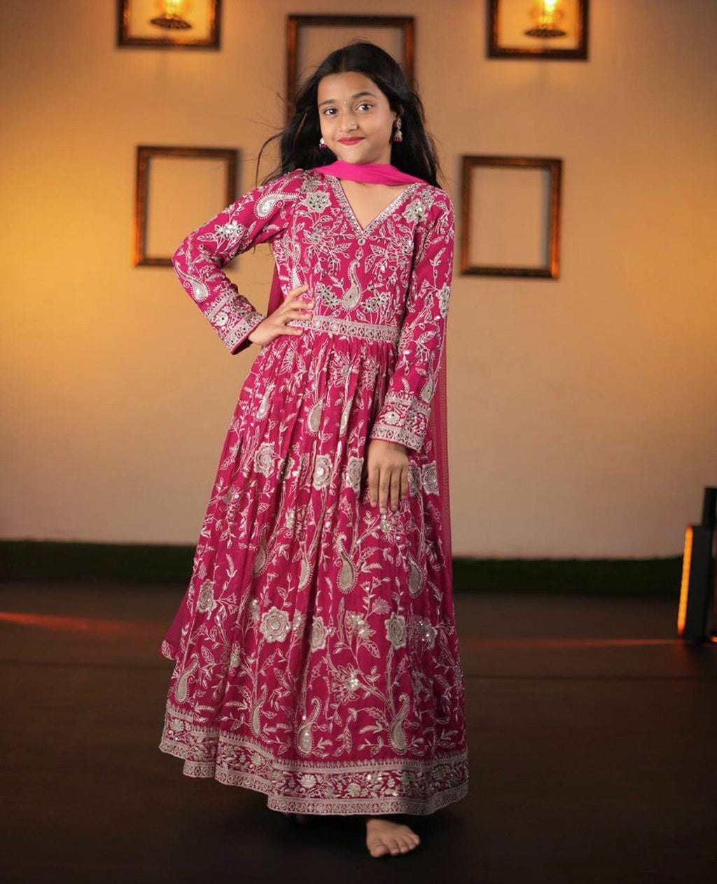 Full-length shot of a young girl smiling in a Fuchsia Pink embroidered Fox Georgette gown.