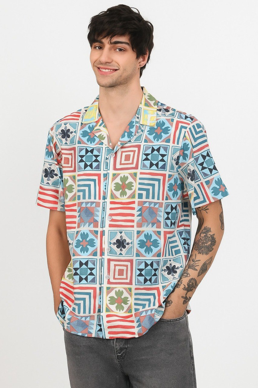 Man in light multi-color geometric squares print Cuban collar shirt, hands in pockets