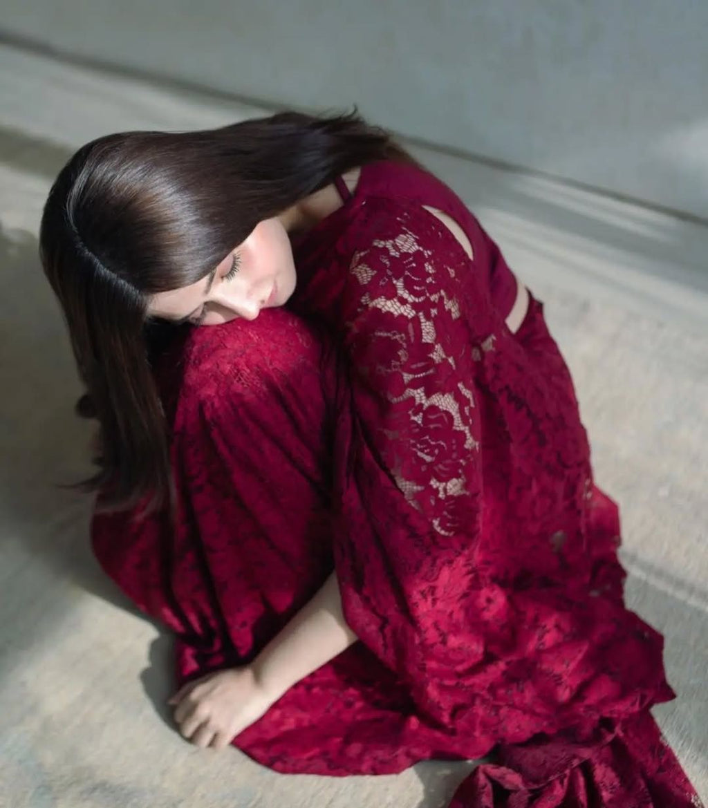 Woman in elegant maroon soft net floral saree, sitting thoughtfully on the floor