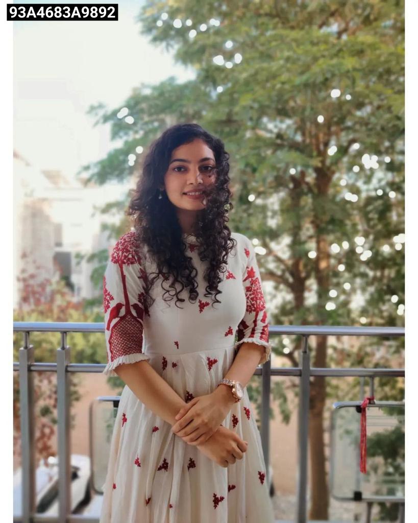 Woman in a white dress with red patterns standing outdoors with trees in the background