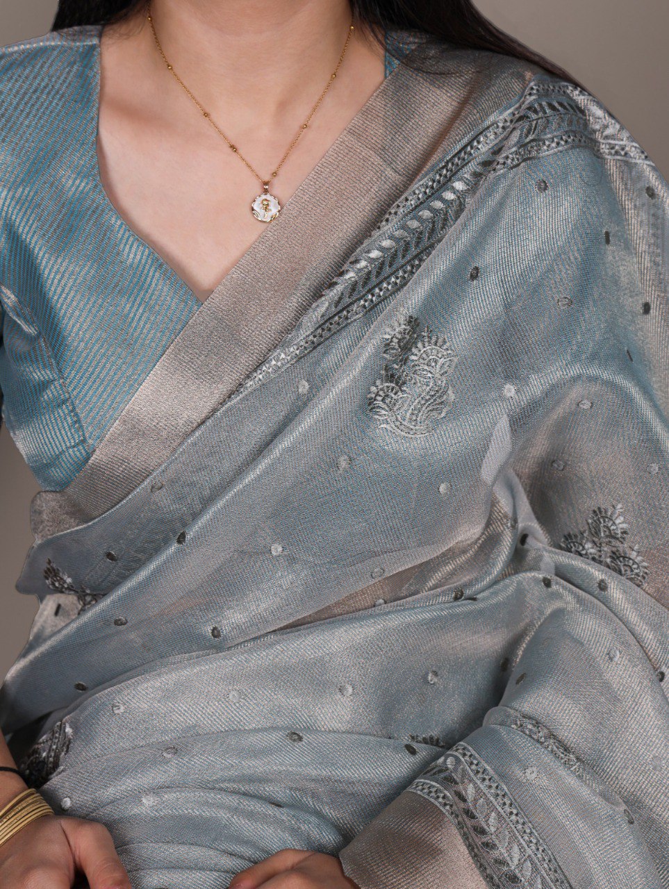Close-up of a model wearing a light blue poly shimmer saree with elegant thread embroidery and delicate polka dot details, gold necklace