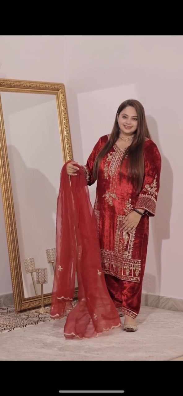 Model wearing a luxurious red velvet patiyala suit with elaborate gold sequence embroidery, holding the matching net dupatta.