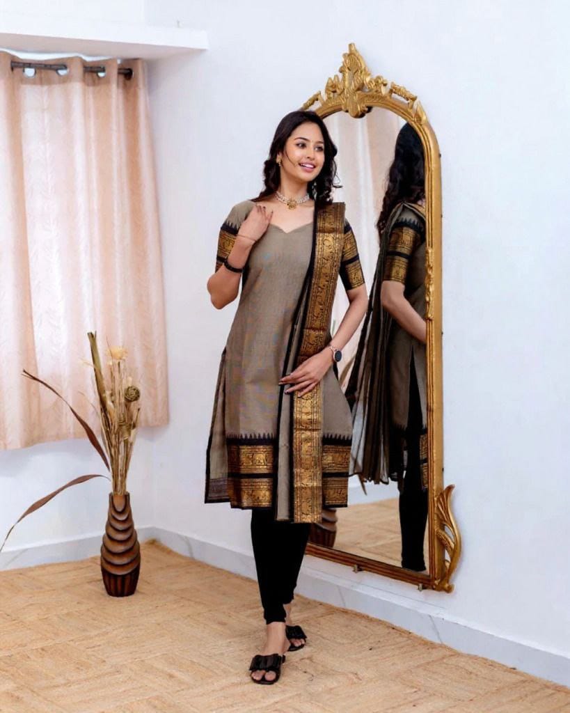 Model showcasing a cream Kanchi Cotton kurti with a golden border dupatta and black leggings, standing by a mirror.