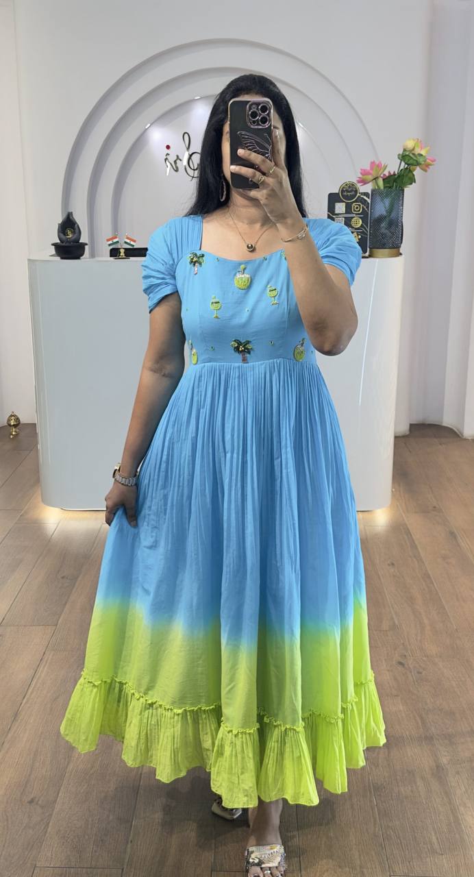 Woman posing in a full-length blue ombre mul cotton maxi dress with coconut handwork and short puff sleeves.
