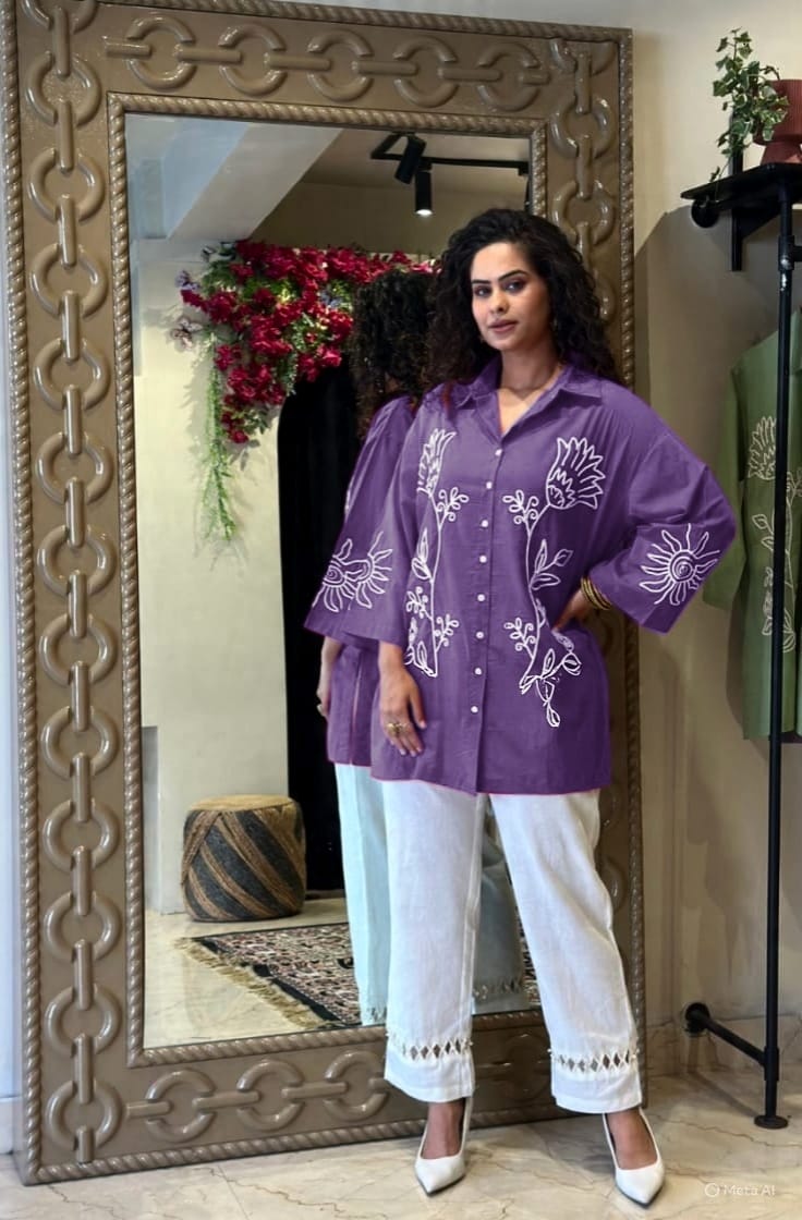 Model in purple embroidered cotton tunic and white pants, posing elegantly in front of a mirror.