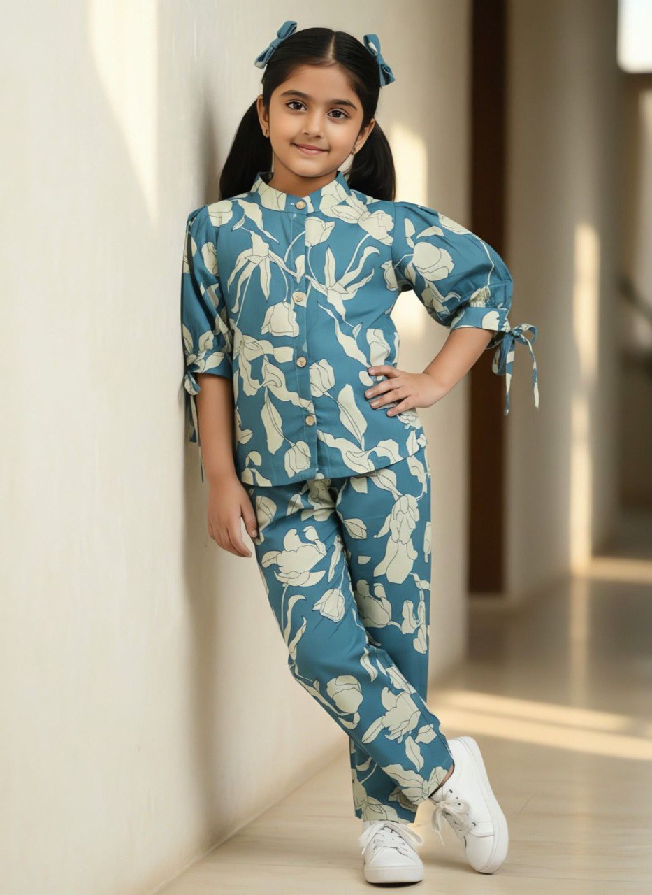 Young girl wearing TRENDBUY blue-green floral soft cotton kurta and pant set, hands on hip, smiling, against a light wall.