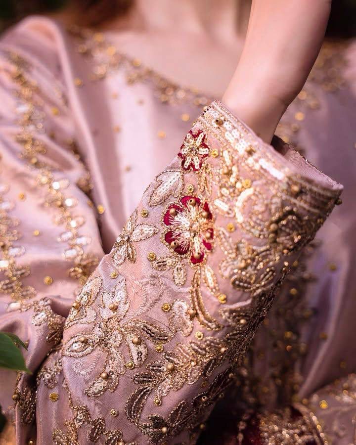 Close-up of a model's arm, showcasing the intricate golden thread and sequin embroidery with red floral patterns on a mauve Chinon silk kurti sleeve.