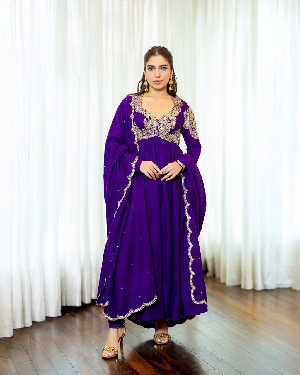 Elegant woman posing in a full-length purple Chinon silk Anarkali gown with golden zari and sequin embroidery, flowing silhouette.