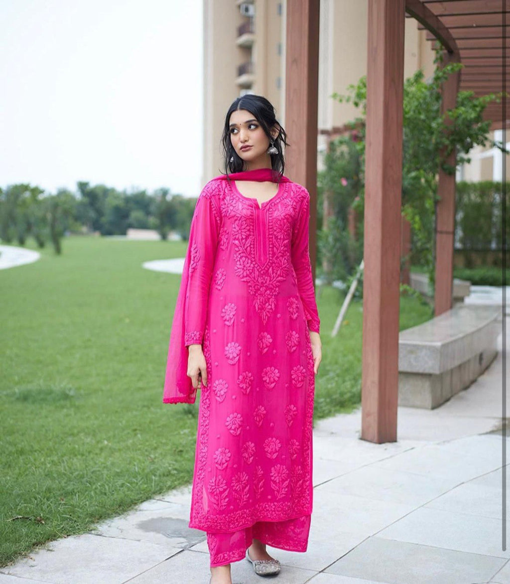 Model posing elegantly in a Hot Pink faux georgette embroidered kurta plazzo suit with matching dupatta, outdoors.
