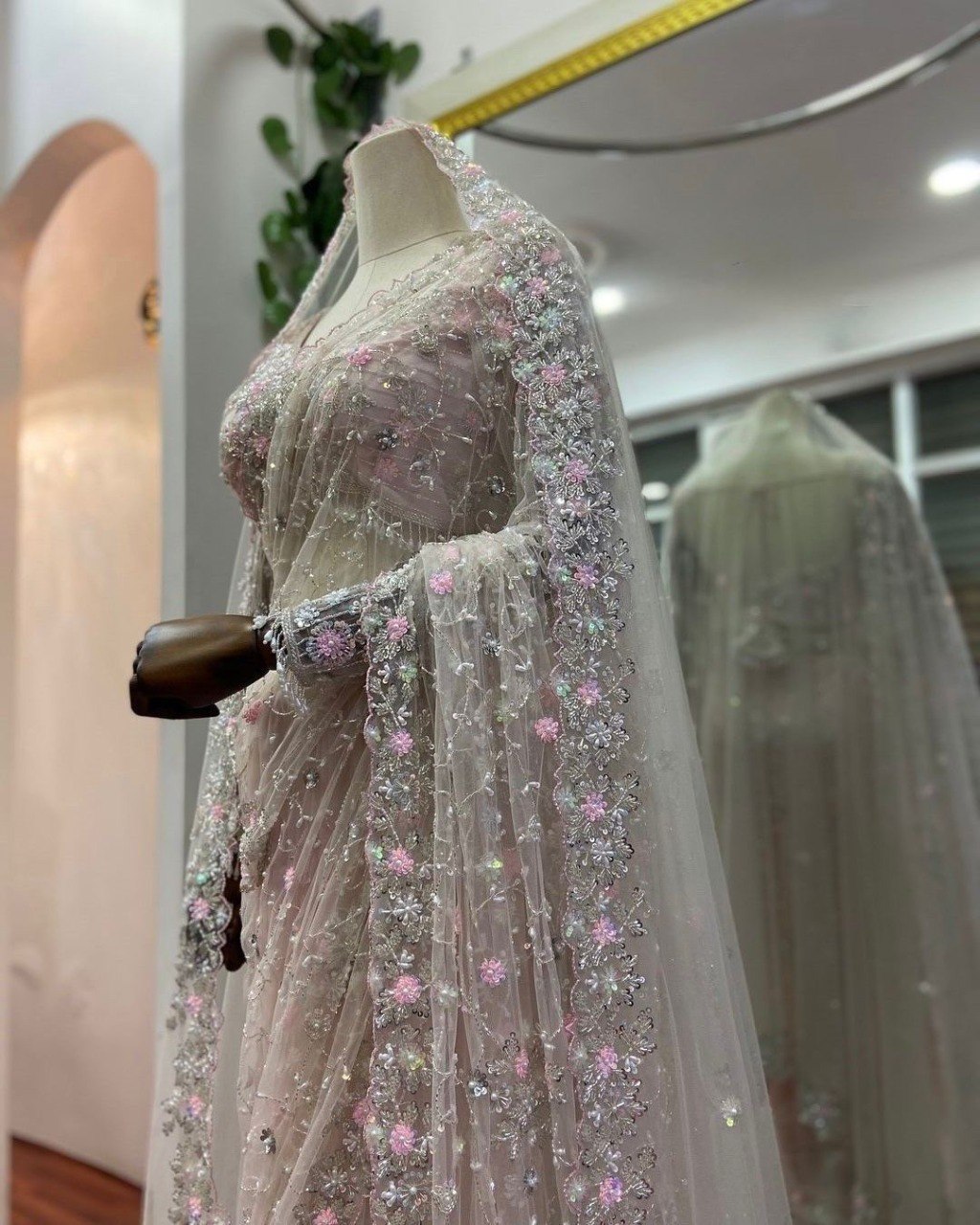 Close-up of blush pink designer net saree with intricate thread and sequin embroidery on mannequin.