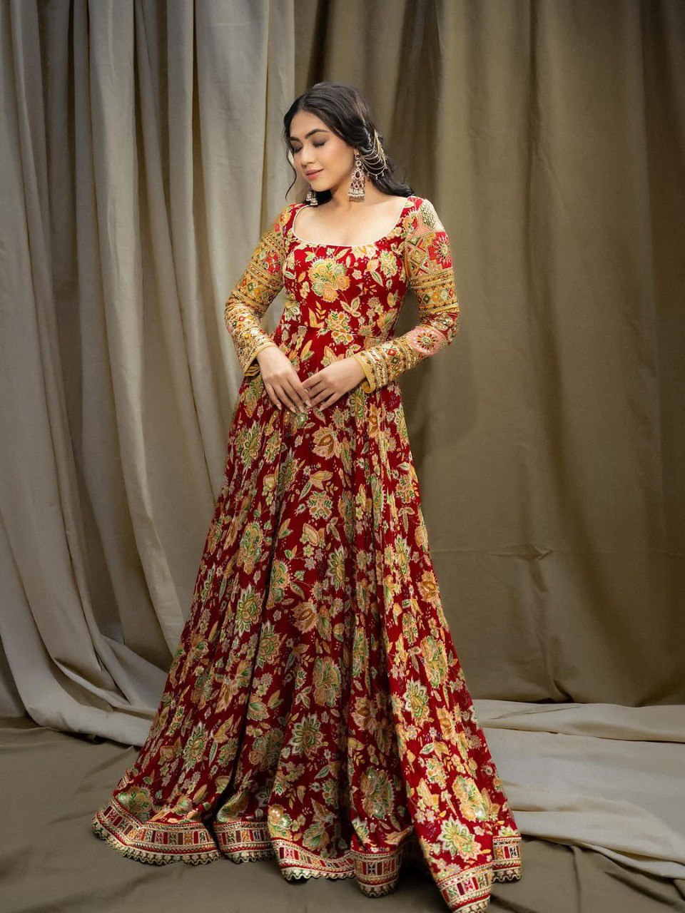 Model posing in a full-length red Chinon silk gown with vibrant floral prints and intricate gold embroidery and sequin work, standing elegantly.