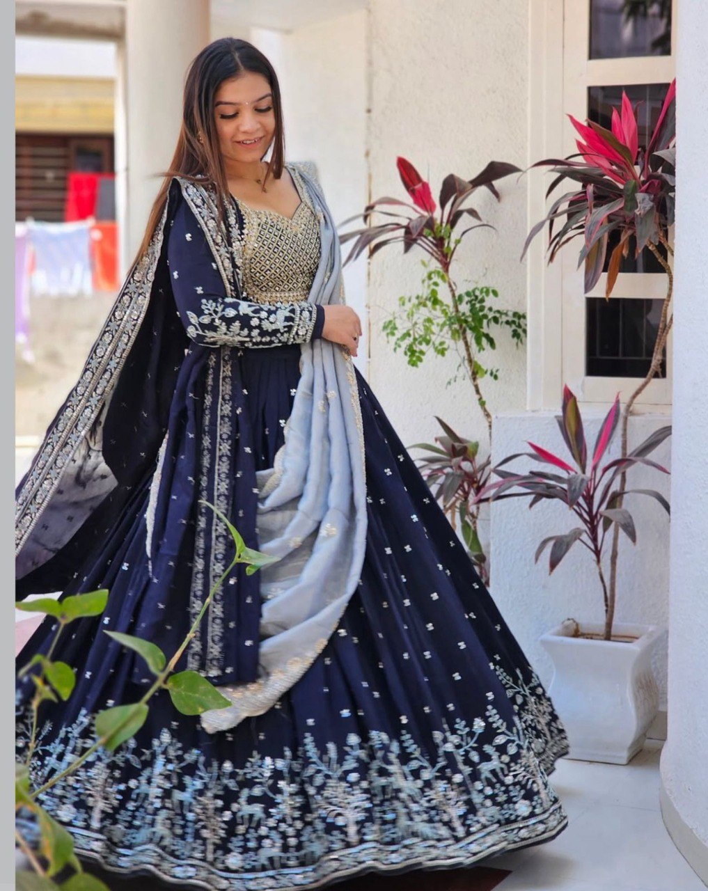 Smiling woman posing gracefully in a navy blue embroidered lehenga choli with a light blue dupatta, outdoors.