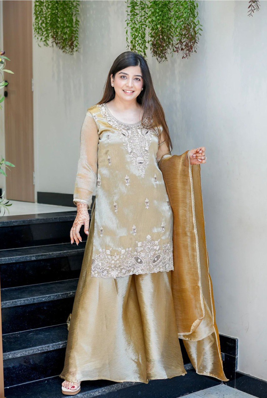 Elegant model posing in a golden Jimmy Choo silk sharara suit with intricate silver embroidery and sequin work, standing on black stairs.