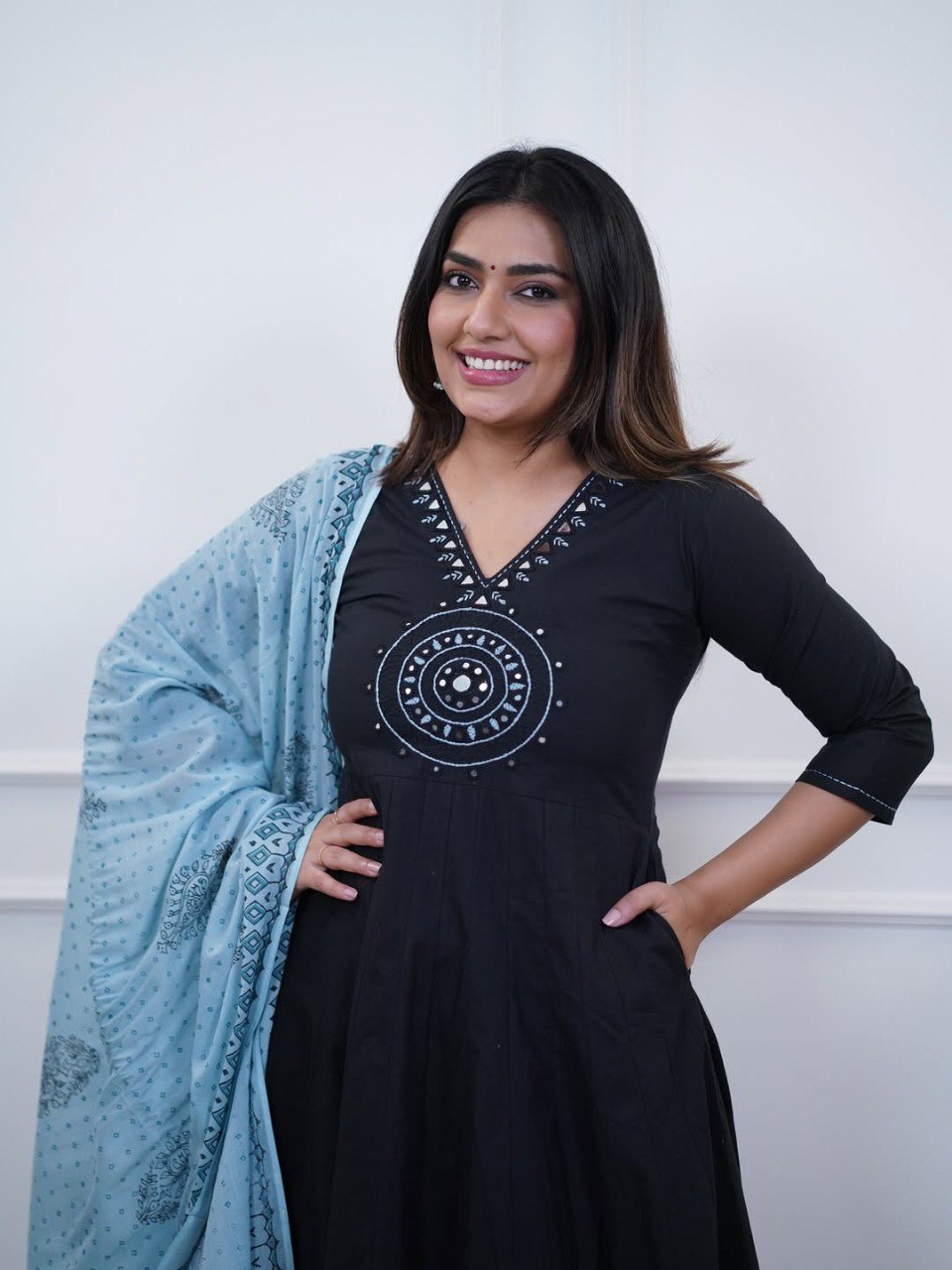 Smiling woman posing in black cotton flex Anarkali suit with blue dupatta, mirror work on yoke