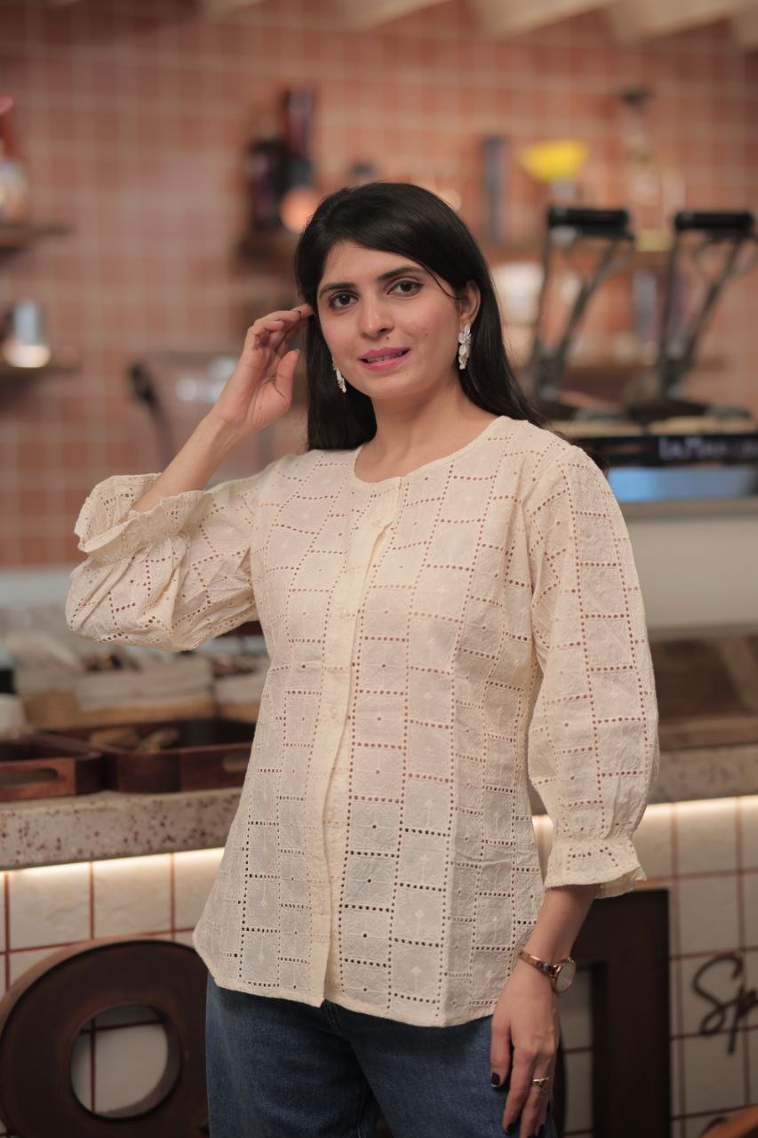 Model posing in cream round neck Schiffli tunic, square embroidery, casual cafe setting.