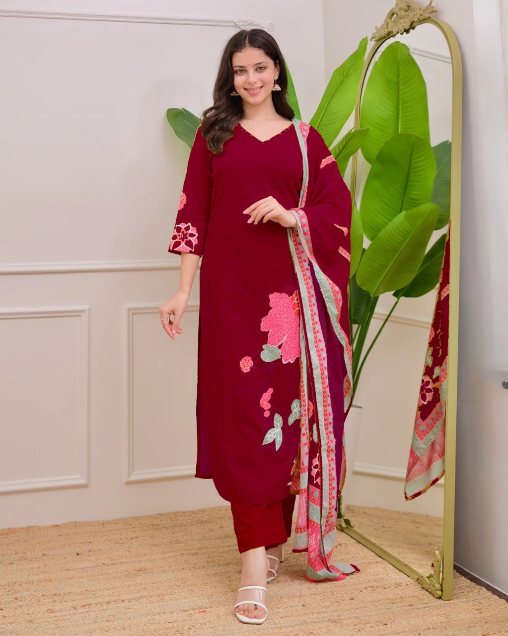 Model in maroon Muslin kurti set, standing elegantly by a mirror with a green plant, smiling.