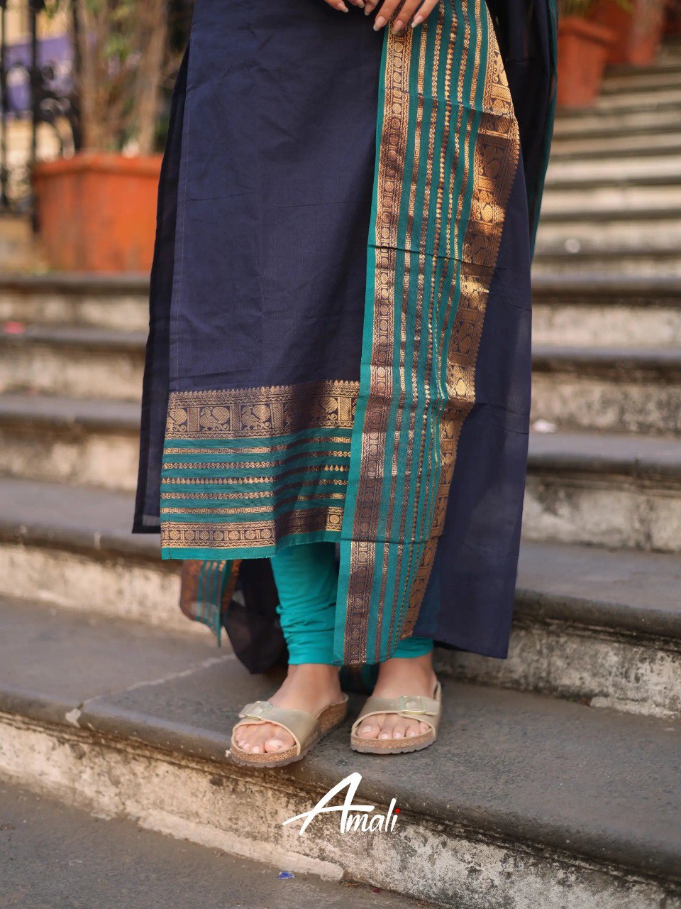 Model's lower body in navy blue Kanchi Cotton kurti and teal leggings, showcasing the ornate gold and teal border on the kurti and dupatta, with golden sandals.