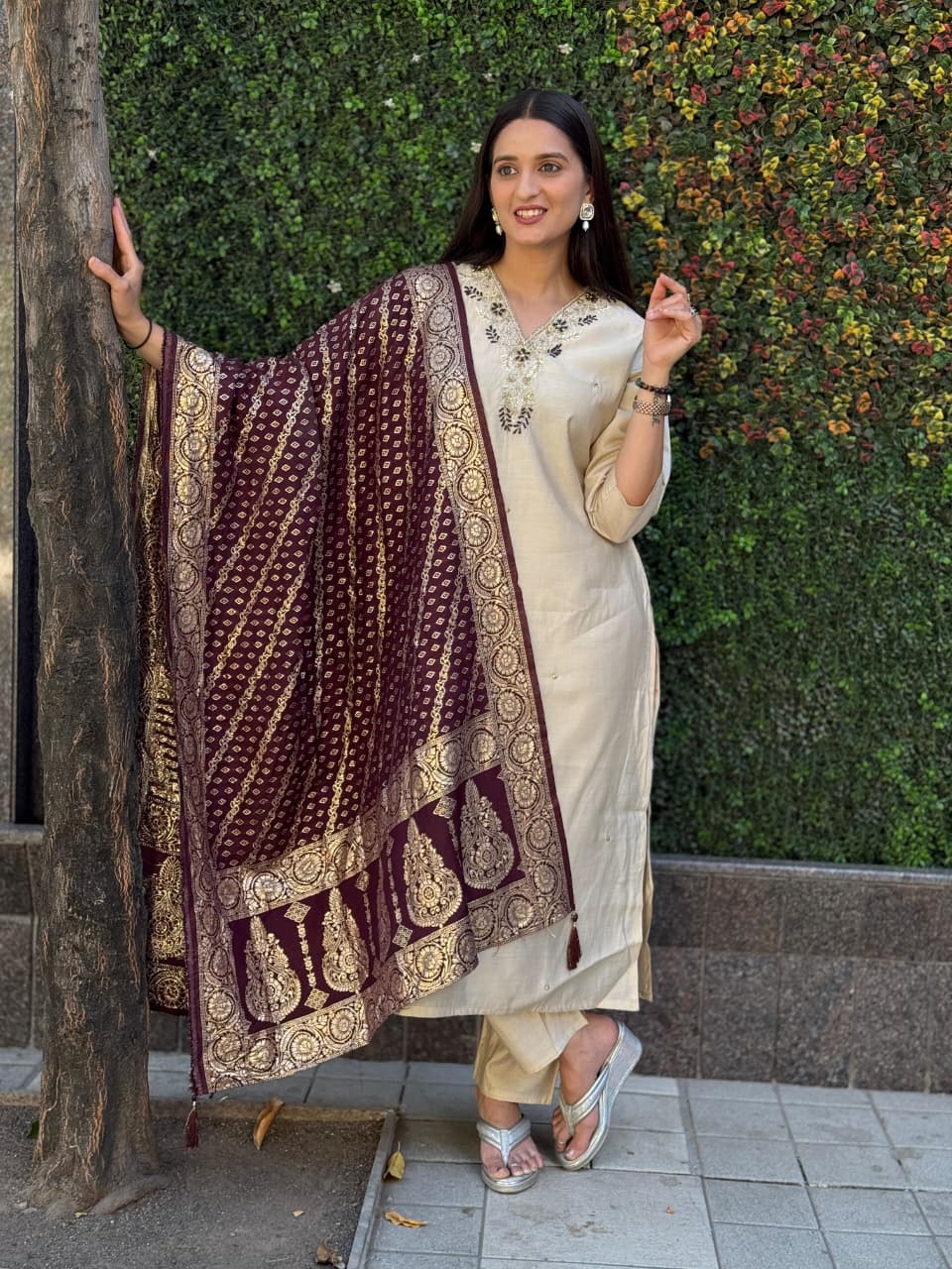 TRENDBUY model in elegant Cream Roman Silk Kurti Pent Dupatta Set with maroon jacquard dupatta and hand work neckline, posing outdoors.