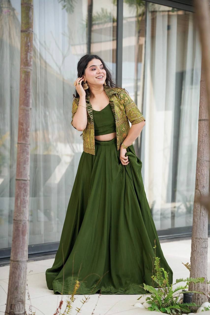 Smiling woman wearing olive green 3-piece lehenga choli with embroidered koti, posing outdoors.