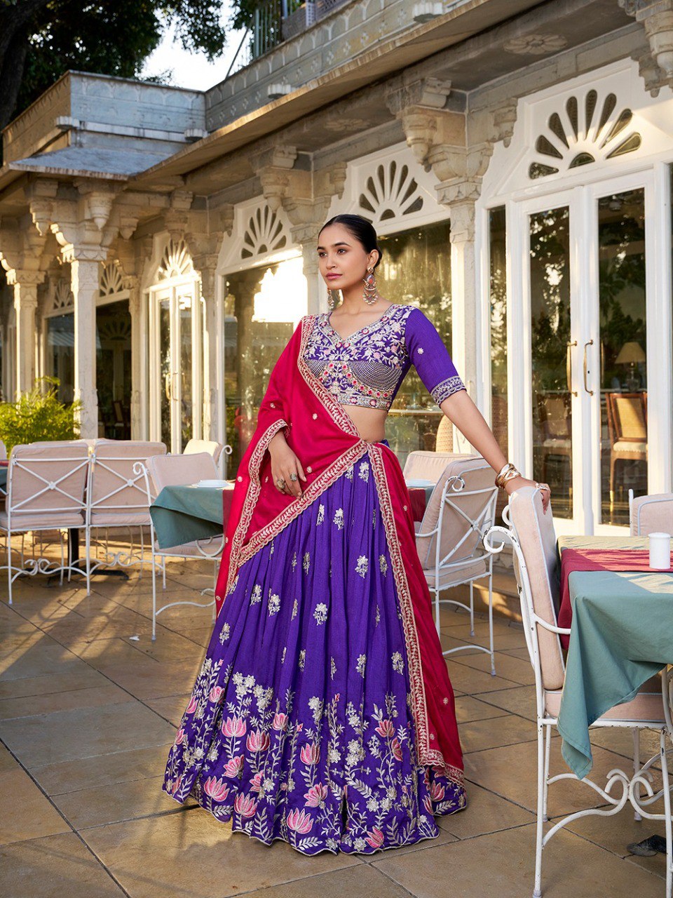 Model in a Regal Purple and Hot Pink Vichitra Silk Lehenga Choli with intricate sequin and thread embroidery, posing elegantly in an outdoor setting.