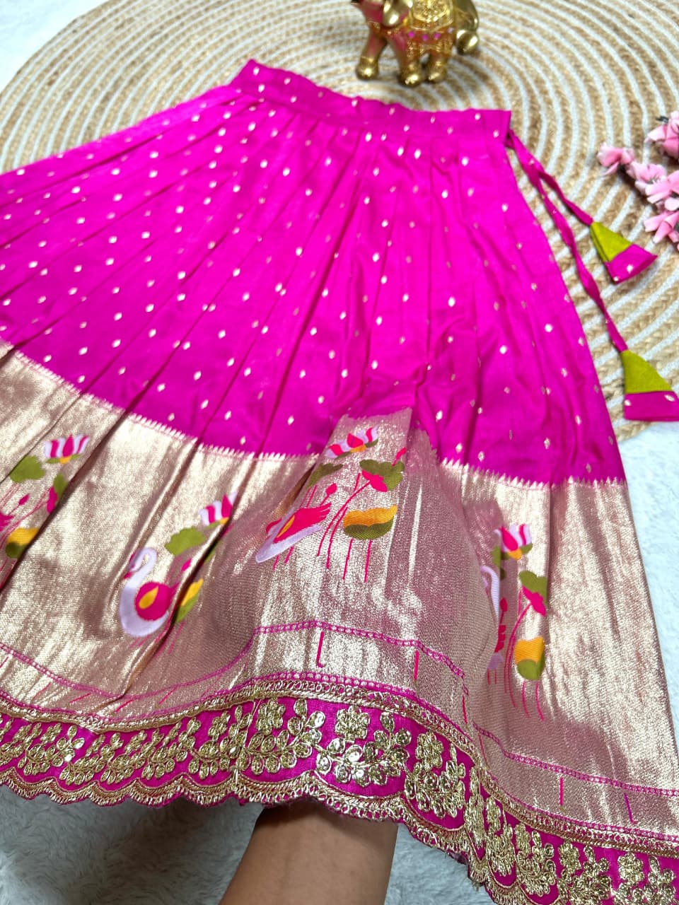 Close-up of a vibrant hot pink kids lehenga skirt with golden zari border and detailed duck and floral patterns.