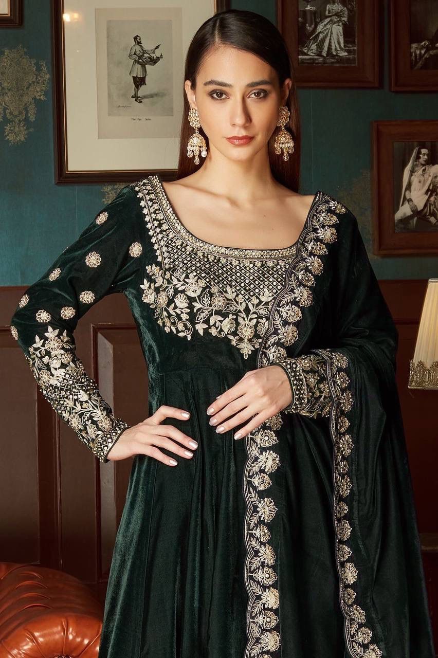 Close-up front view of model in emerald velvet Anarkali gown, highlighting intricate gold embroidery on bodice, sleeves, and dupatta trim.