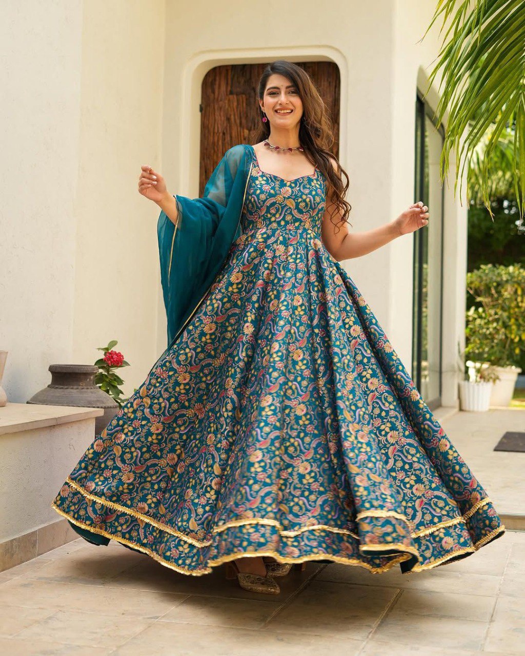 Full shot of woman smiling in a teal digital printed Anarkali gown with an 8-meter flair, holding a two-tone organza dupatta.